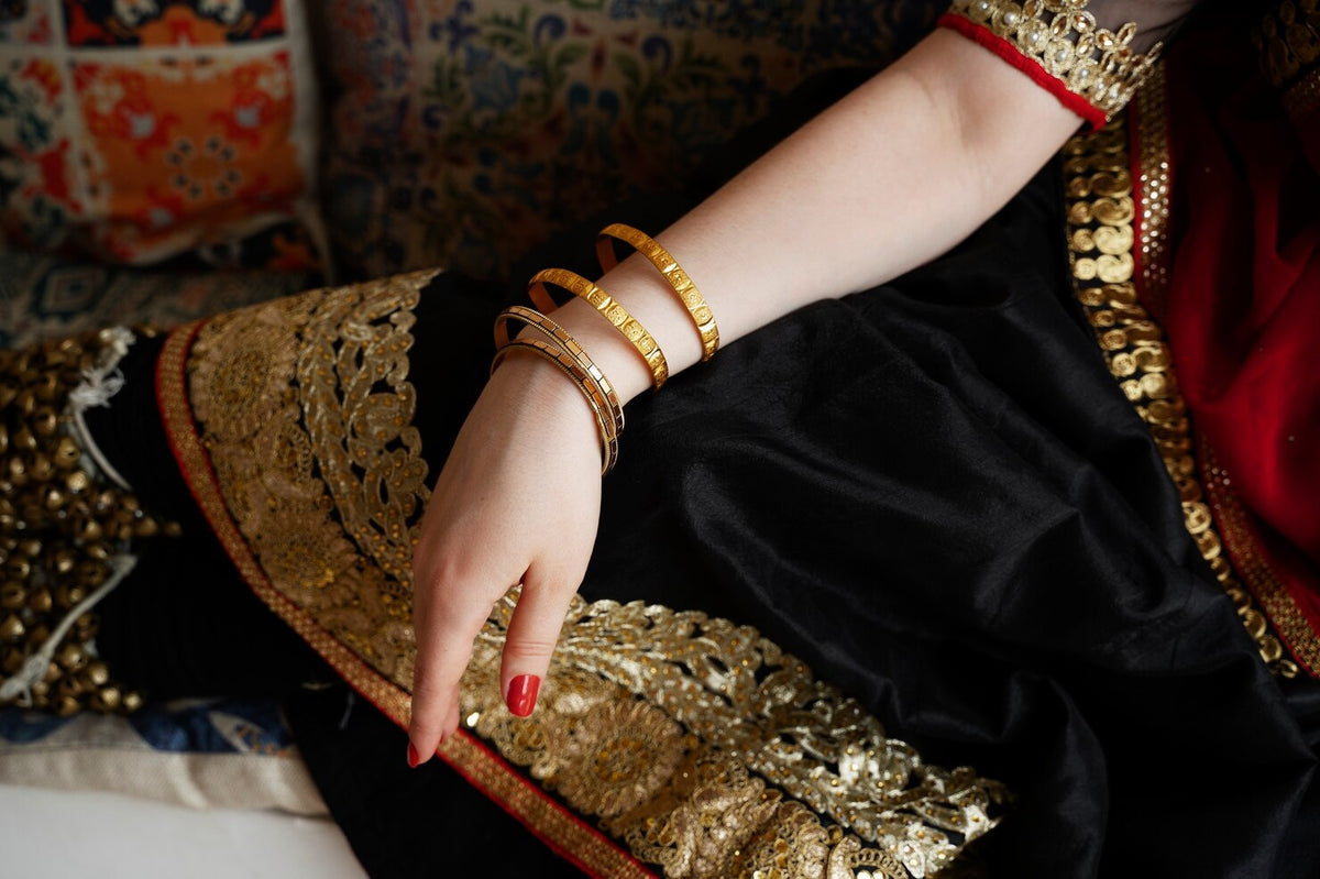 Woman wearing stacked gold bangles on her wrist against a black and gold embroidered saree