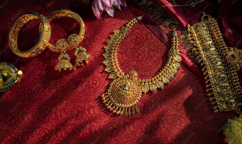 Traditional South Indian temple jewellery set including gold necklace, bangles, jhumka earrings and waist belt on red silk fabric